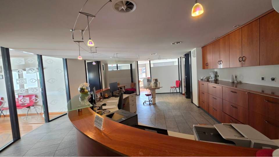 Kitchenette et salon de bureau modernes avec placards en bois, comptoir incurvé et grandes fenêtres donnant sur la ville.