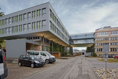 Steinhaus mit rotem Ziegeldach und Dachgauben in einer ruhigen Wohnstrasse unter blauem Himmel.