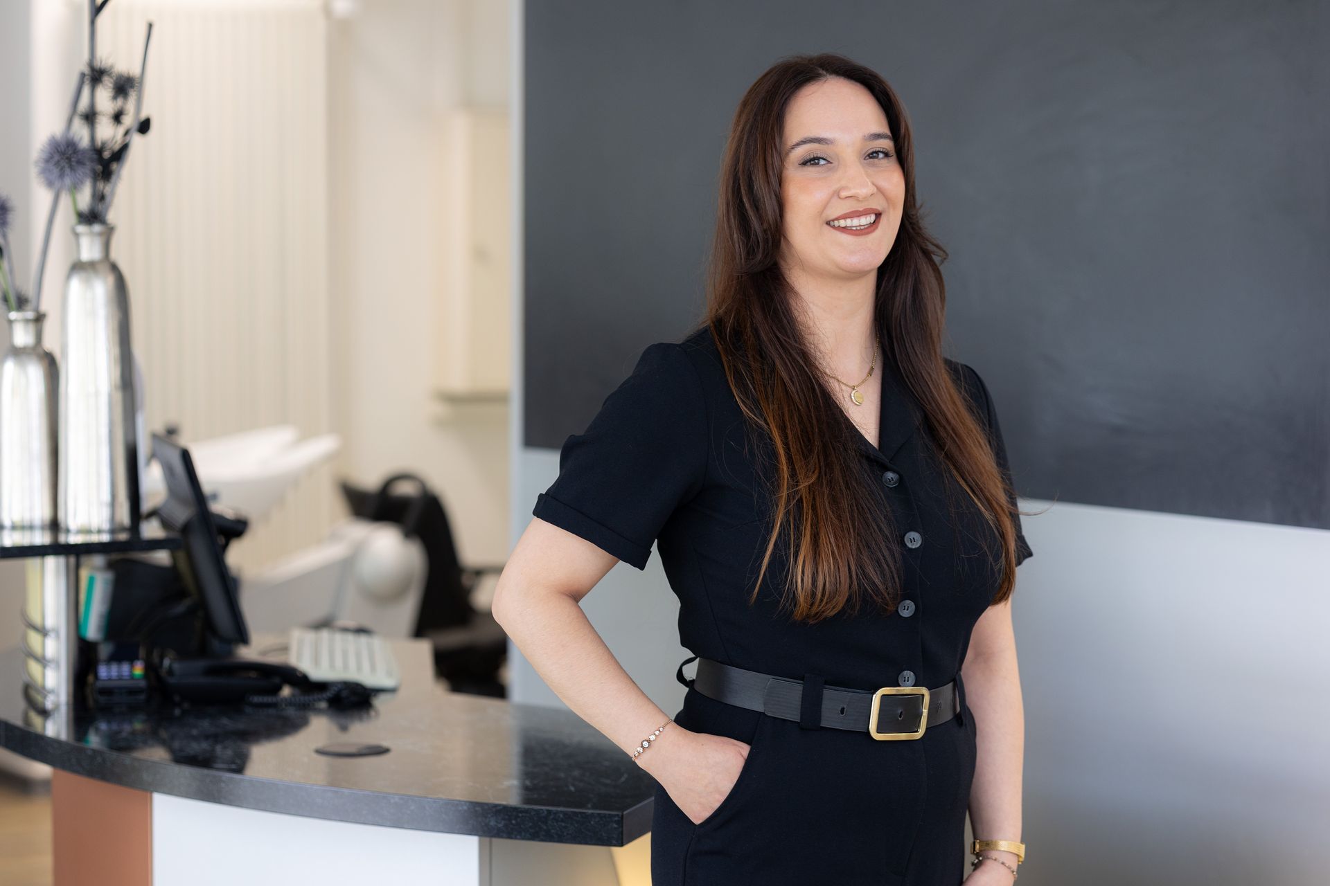 Lächelnde junge Frau mit braunen Haaren und Perlenohrringen.