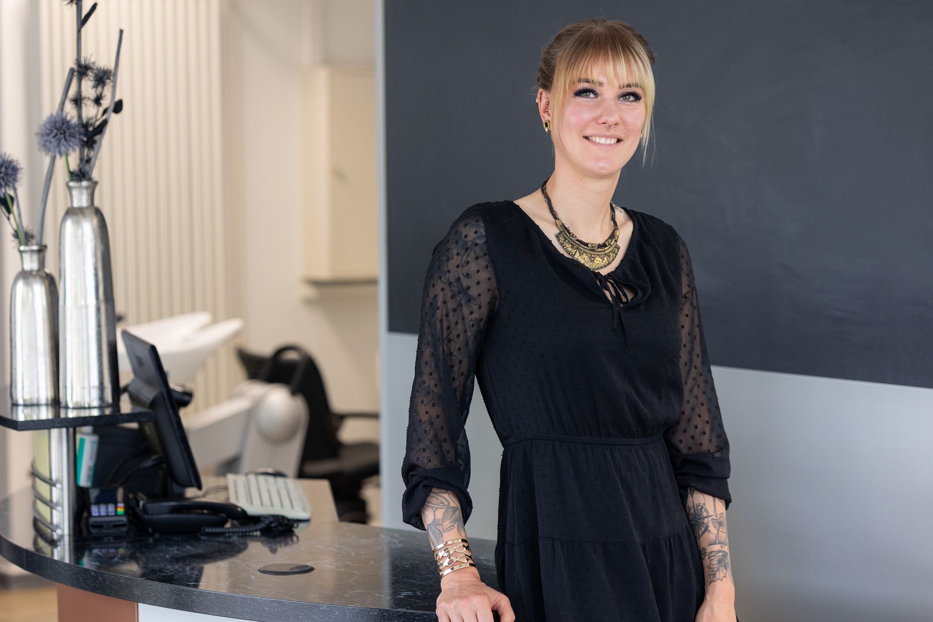 Frau mit blondem Bob lächelt leicht vor einem Fenster.