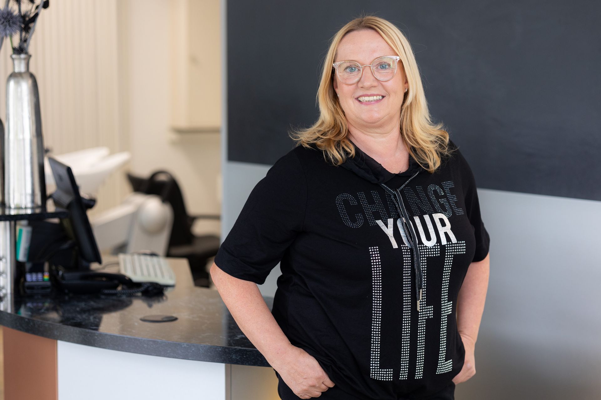 Lächelnde junge Frau mit braunen Haaren und Perlenohrringen.