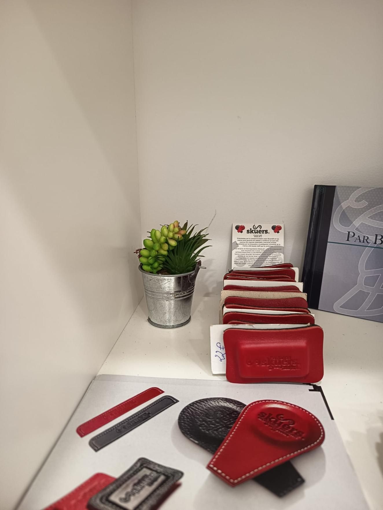 Exhibición de herramientas para uñas rojas y negras en un estante blanco con una pequeña planta en maceta y cajas.