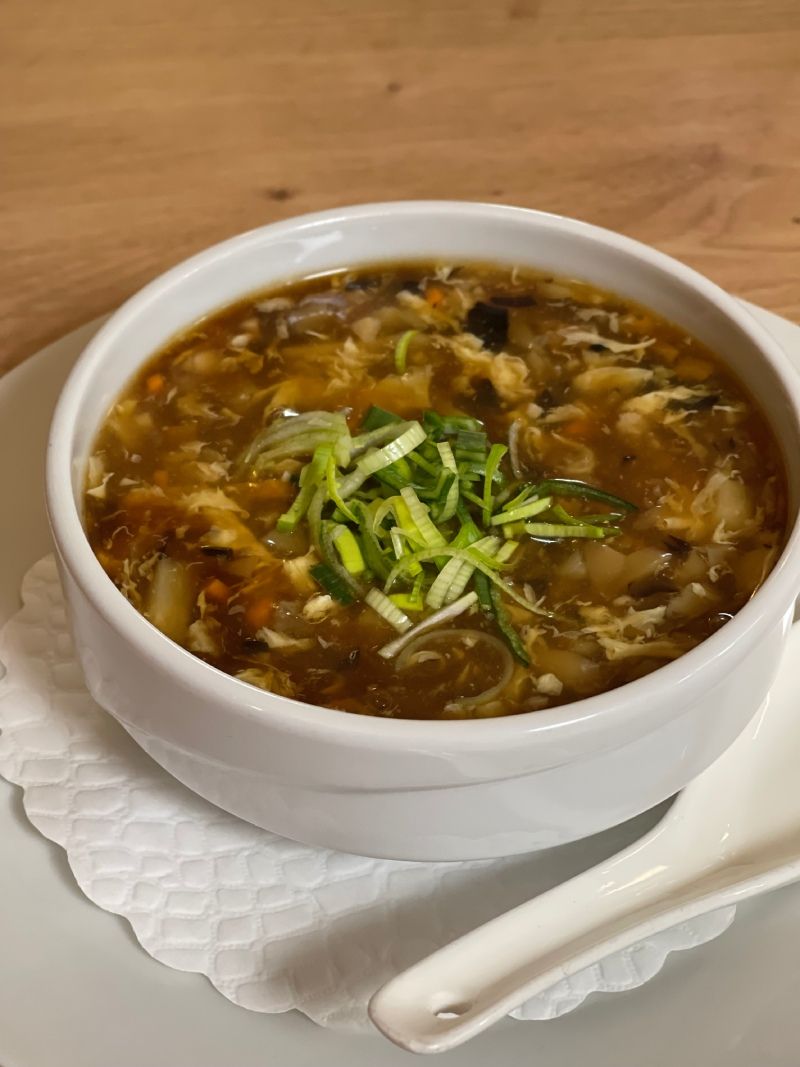 Un bol de soupe avec des oignons verts et une cuillère sur une assiette.