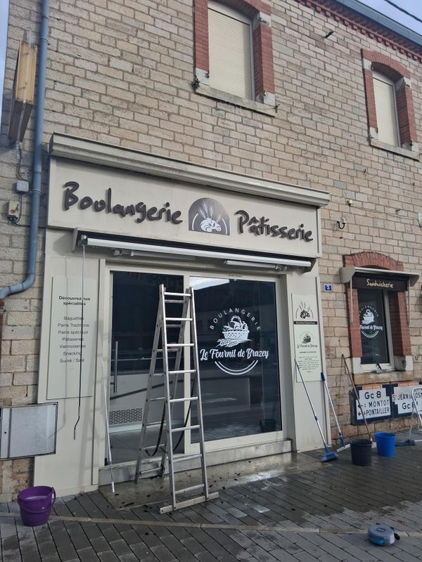 Boulangerie-pâtisserie en façade, avec porte ouverte et échelle extérieure, façade en briques et enseignes.