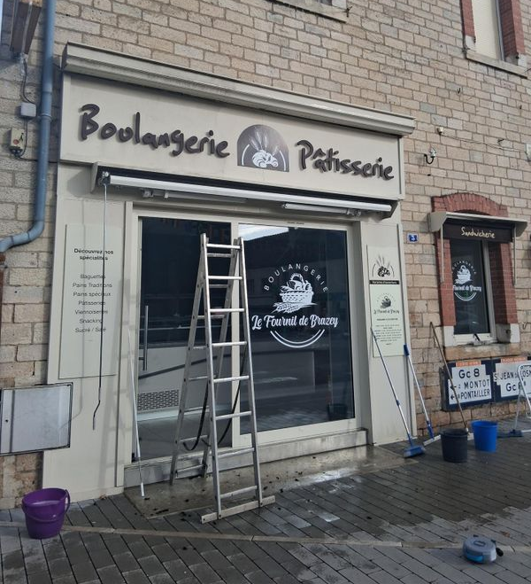 Façade de boulangerie avec une échelle appuyée contre l'entrée et un seau sur le trottoir devant.