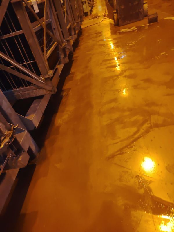Un sol industriel humide, éclairé d'une lumière jaune, jouxtant des étagères métalliques et des équipements.