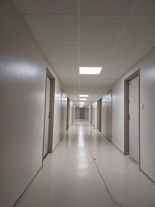 Couloir blanc vide avec des portes des deux côtés et un sol fissuré éclairé par des néons.