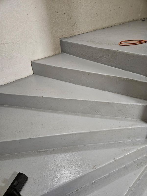 Escalier en colimaçon en béton avec marches gris clair et câble orange enroulé sur le palier.