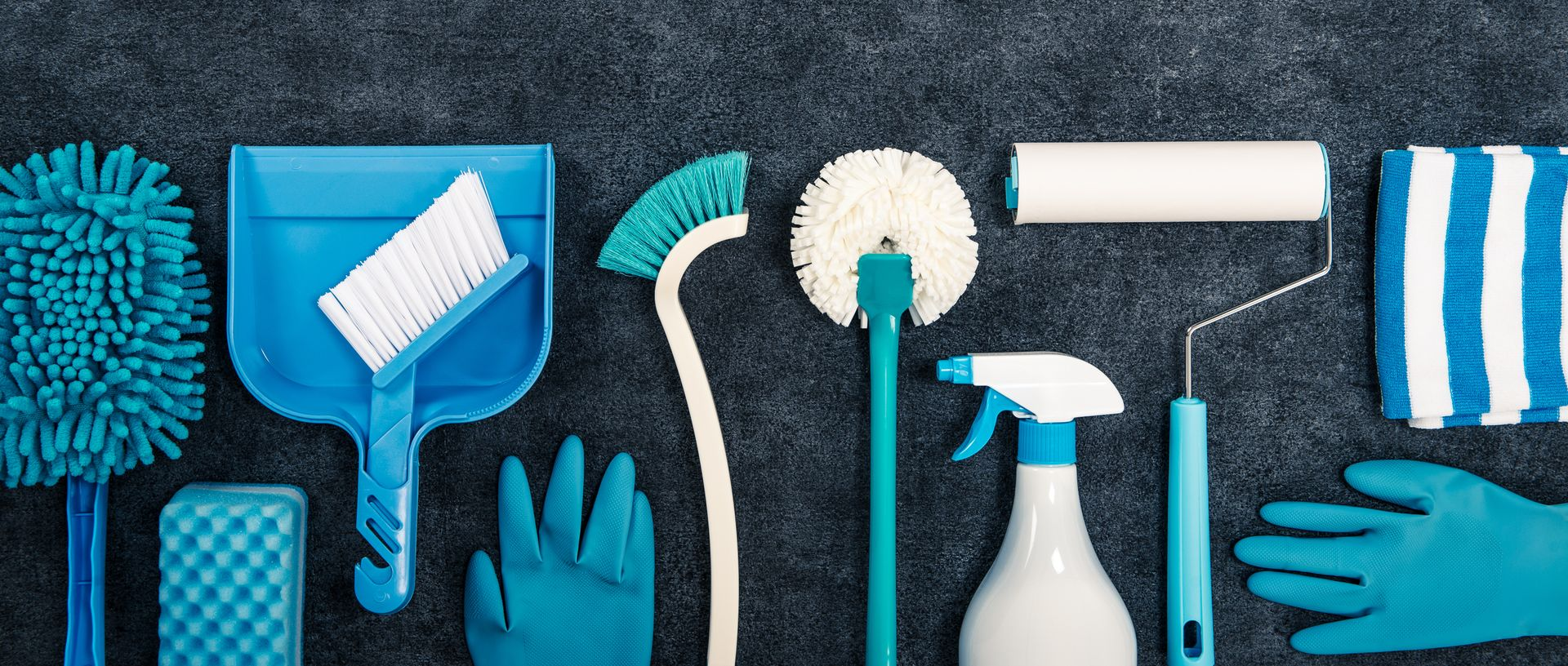 Outils et produits de nettoyage bleus disposés en rangée sur un fond sombre.