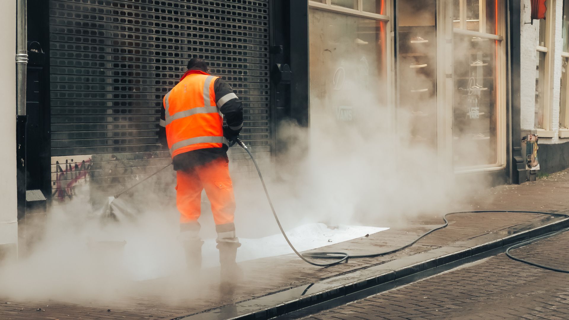 Un ouvrier en tenue de sécurité orange découpe le bitume, provoquant poussière et vapeur dans une rue de la ville.
