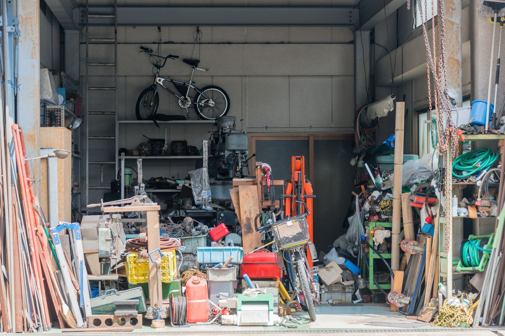 Atelier-garage encombré d'outils, d'équipements et d'un vélo rangés sur des étagères et à même le sol.