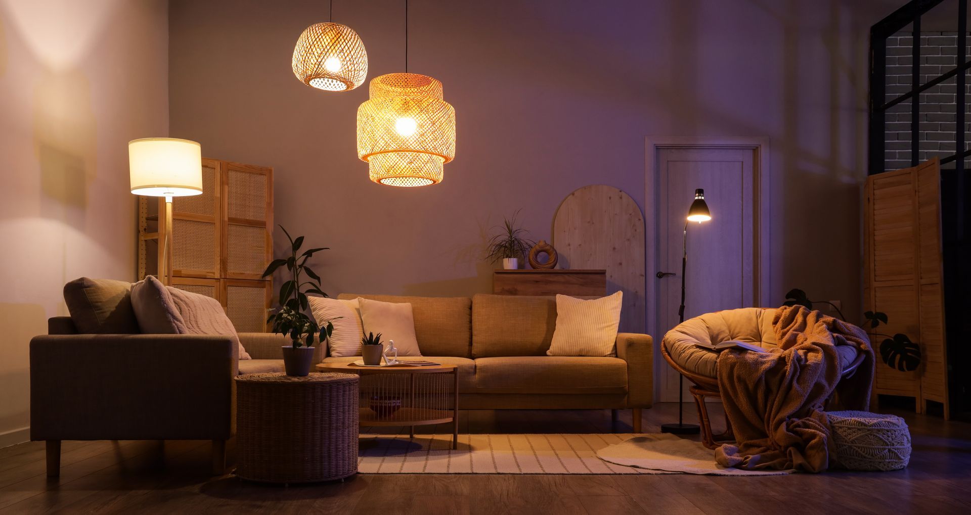 Salon cosy avec éclairage chaleureux, canapé beige, lampes en osier, chaises et plantes décoratives.