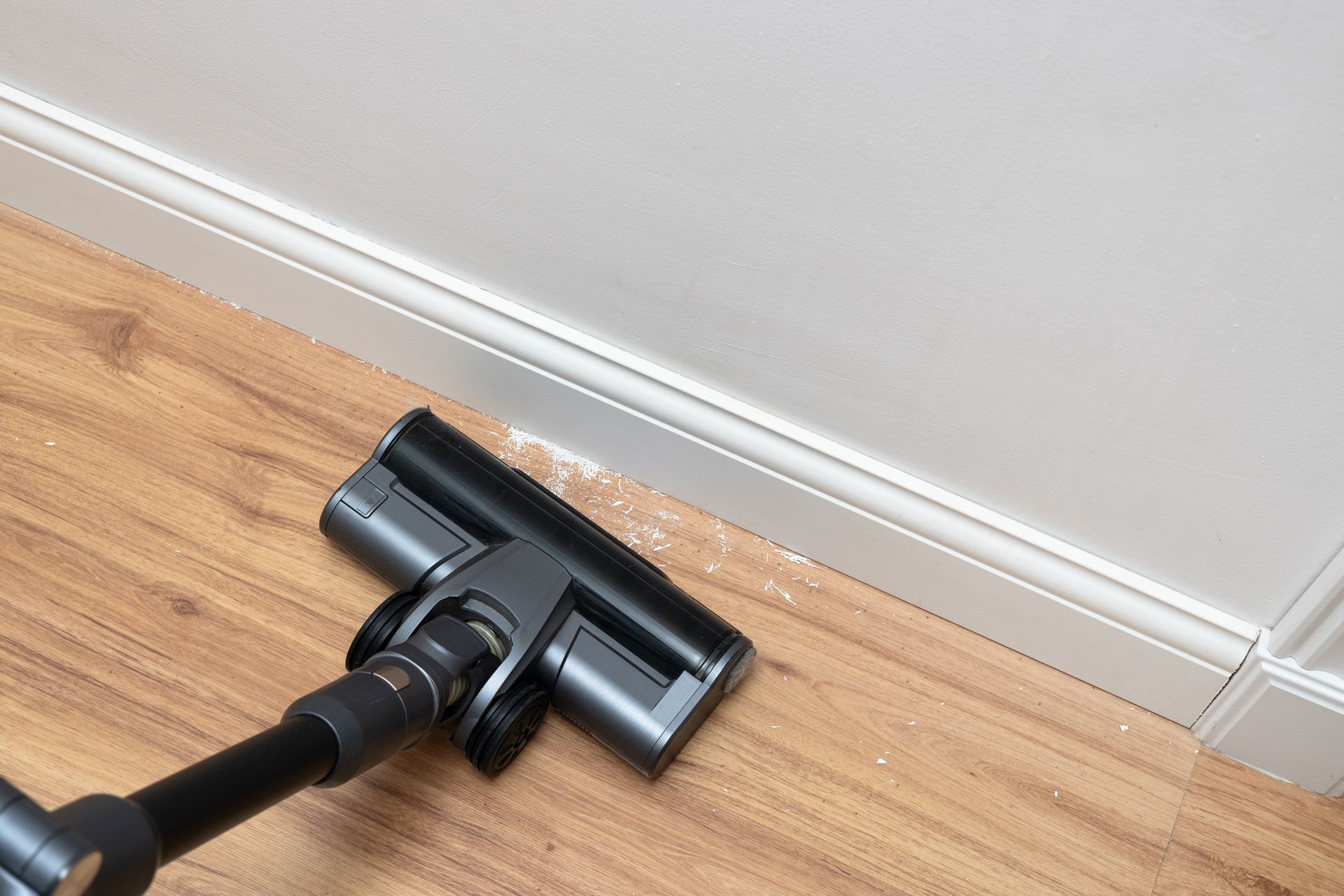 Tête d'aspirateur noire sur un parquet clair, à côté d'une plinthe blanche.