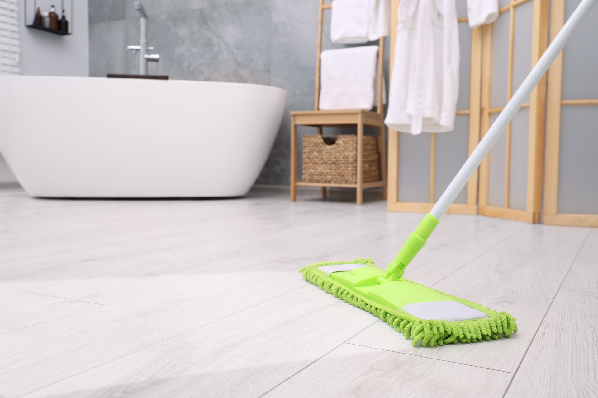 Une serpillière verte sur le sol blanc d'une salle de bain, à côté d'une baignoire et de serviettes.