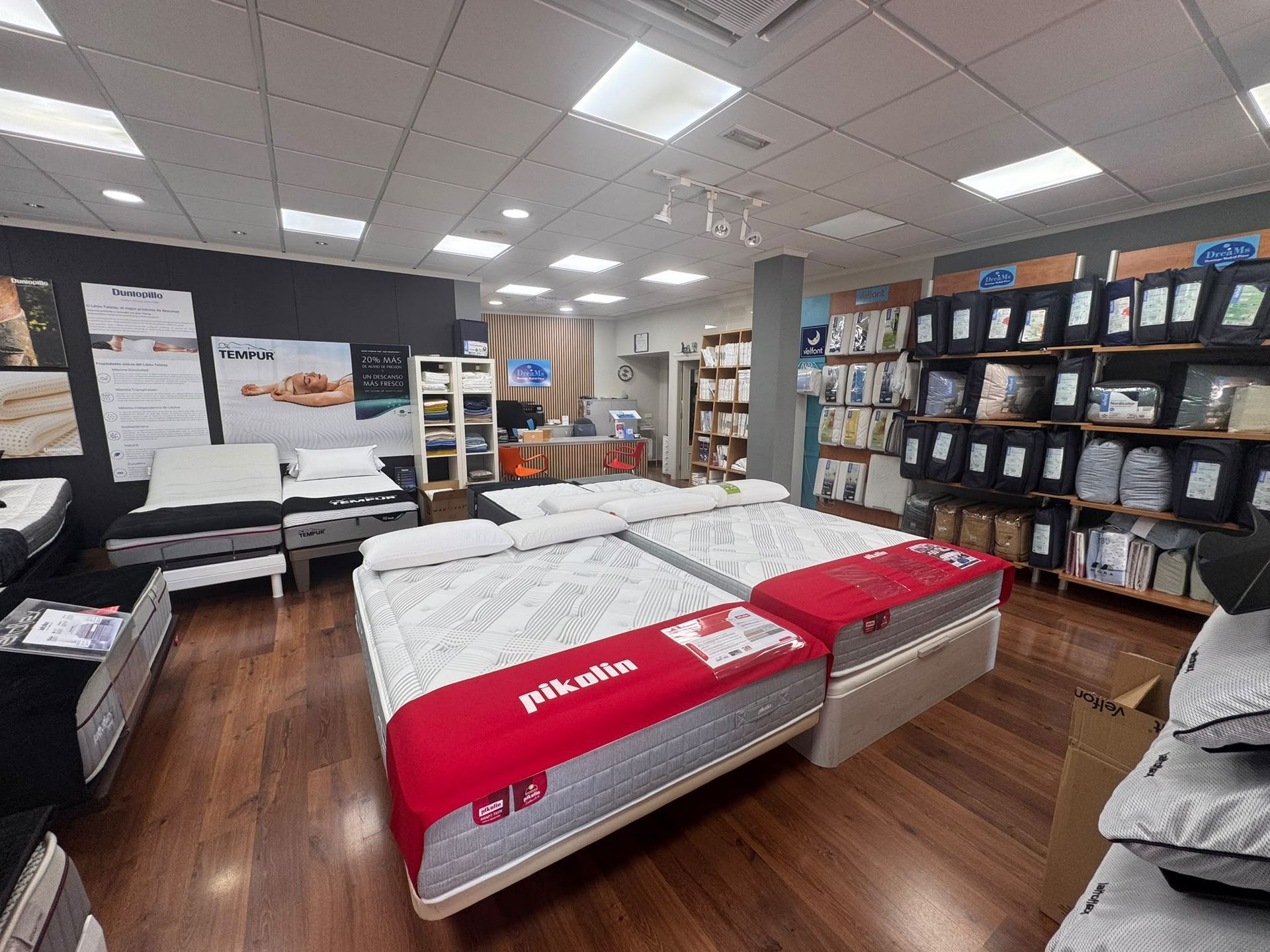 Sala de exposición de colchones con camas de muestra, pósteres y estanterías con accesorios de cama.