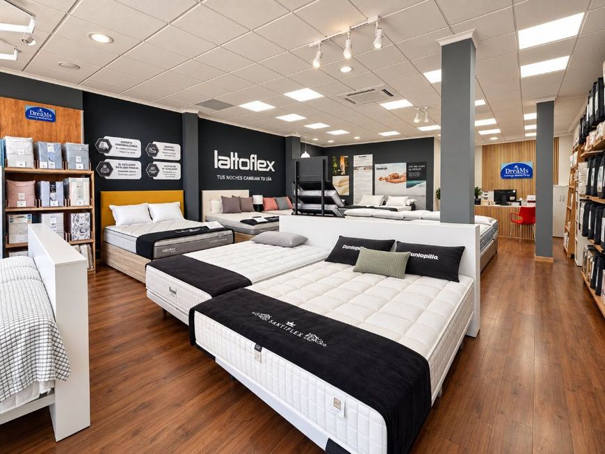Sala de exposición de una tienda de colchones con varias camas, vitrinas en blanco y negro y suelo de madera.