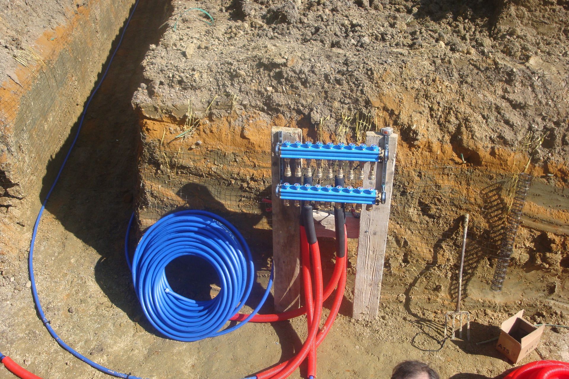 Des tubes bleus et rouges sont reliés à un collecteur bleu dans une excavation.
