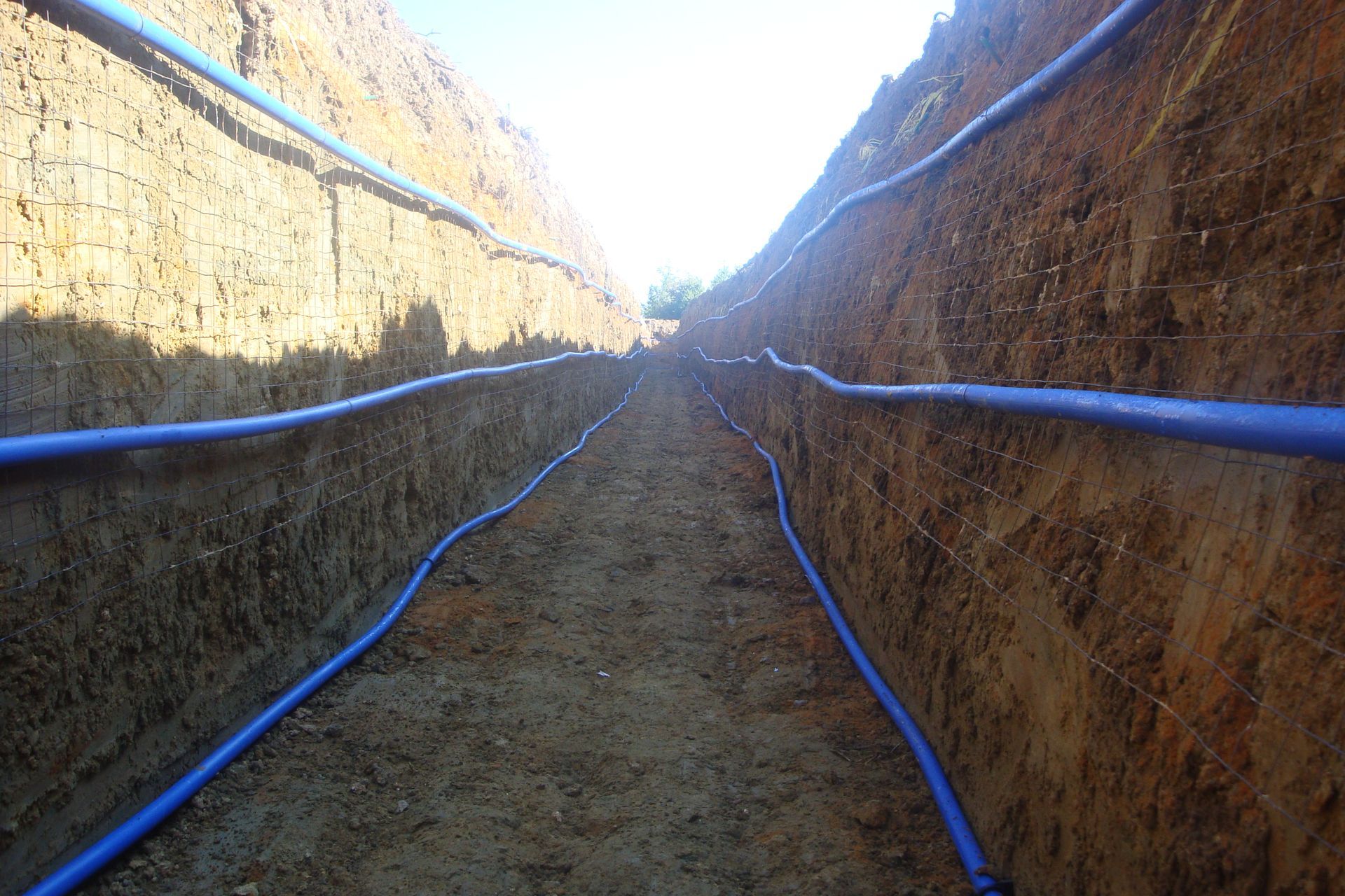 Longue tranchée avec des tuyaux bleus installés à l'intérieur.