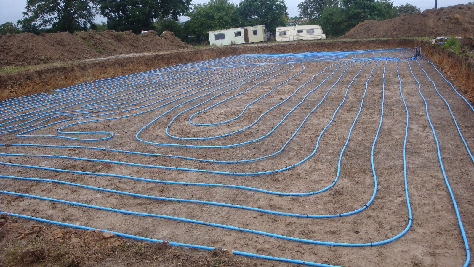 Des tubes bleus d'un système géothermique disposés en grille sur un terrain excavé.