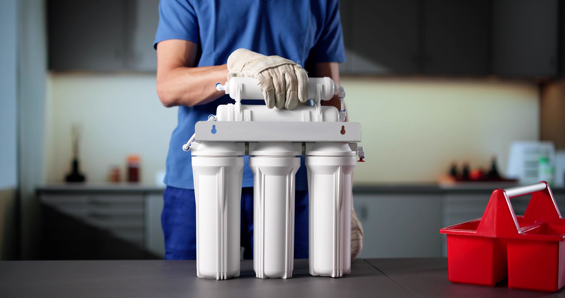 Personne tenant un système de filtration d'eau blanc avec trois cartouches verticales.