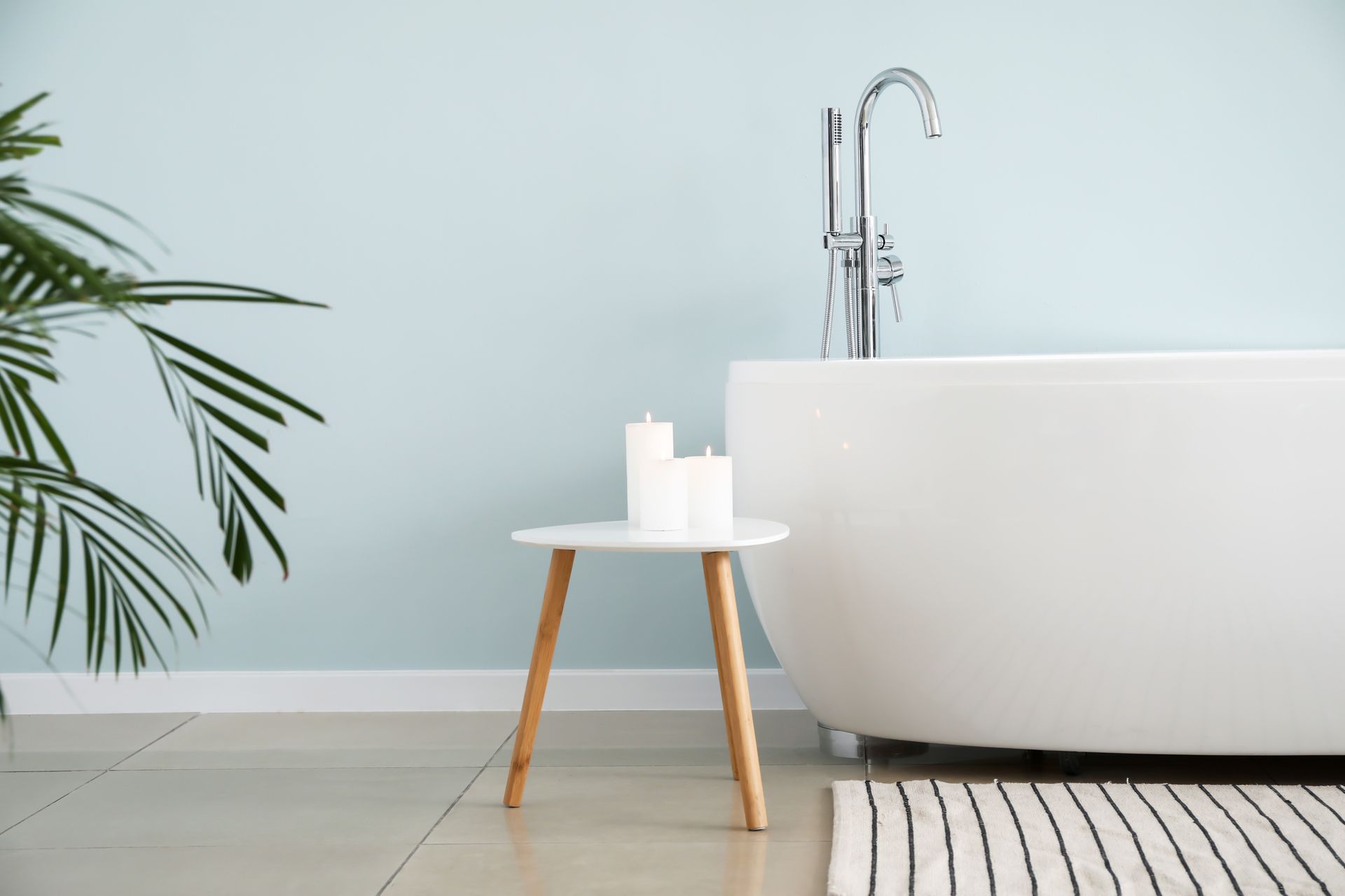 Baignoire blanche avec robinet argenté, petite table avec des bougies.