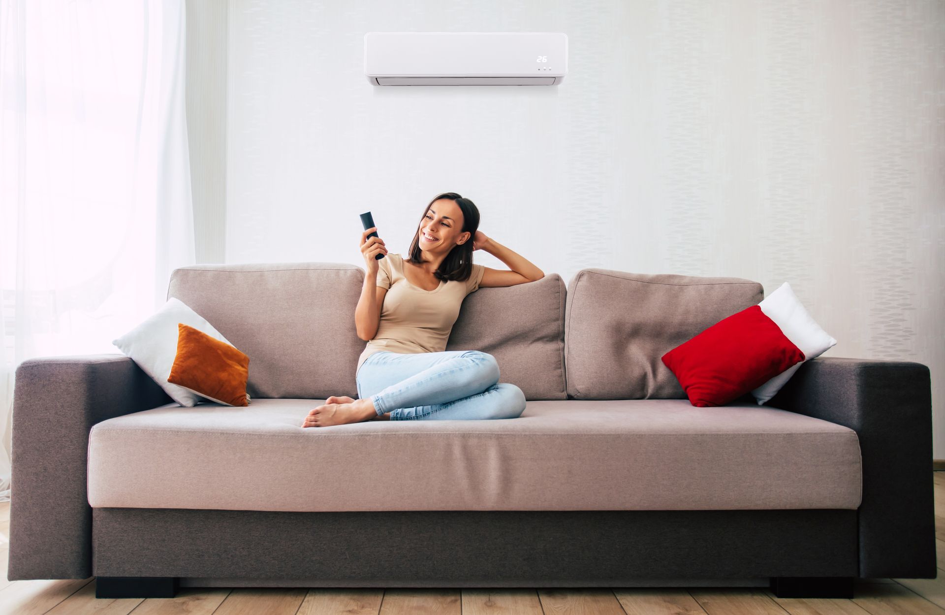 Une femme assise sur un canapé, télécommande en main, climatiseur au-dessus.