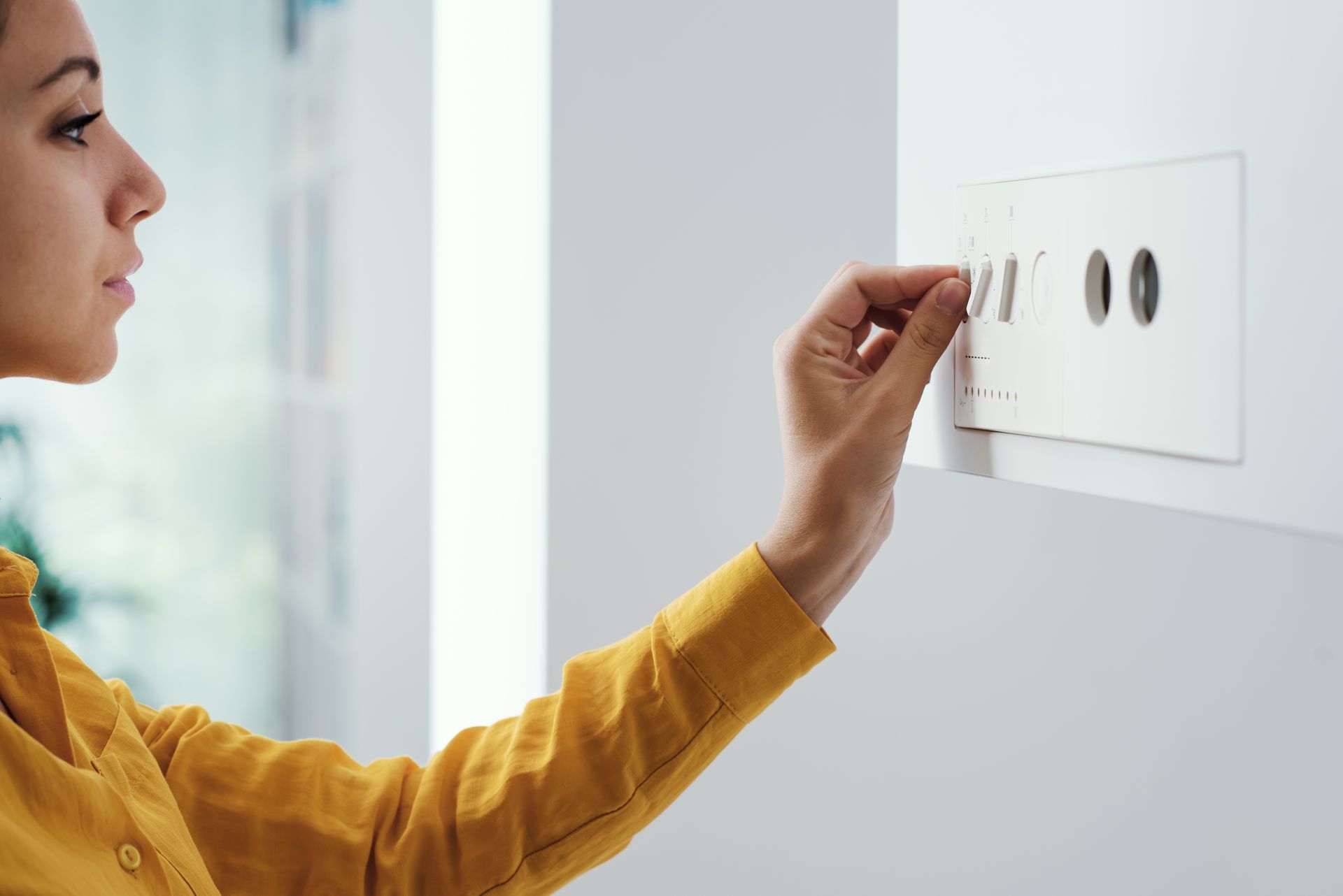 Femme en chemise jaune réglant un thermostat mural blanc.