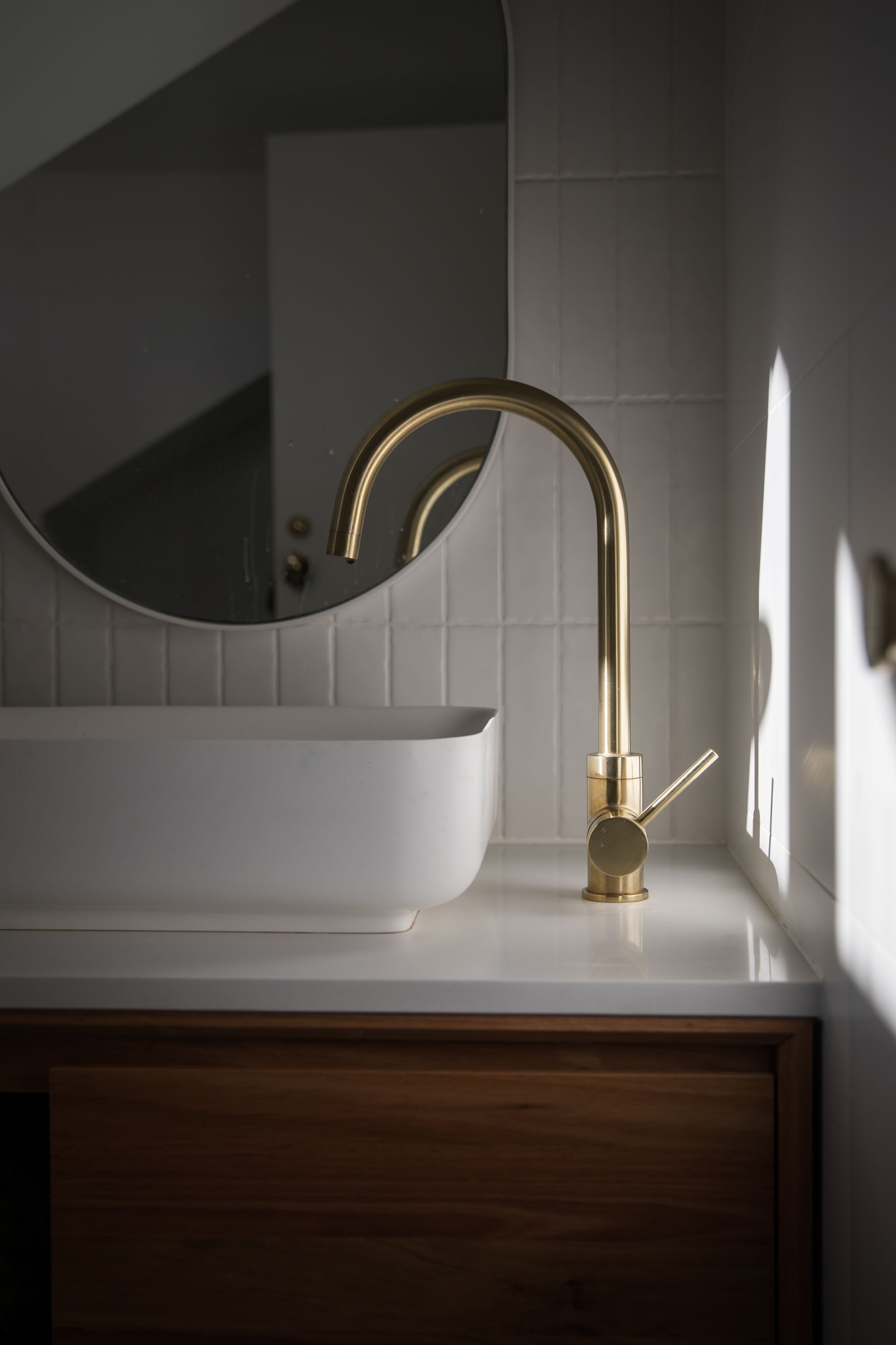 Robinet doré, miroir rond et un lavabo blanc dans une salle de bains moderne.