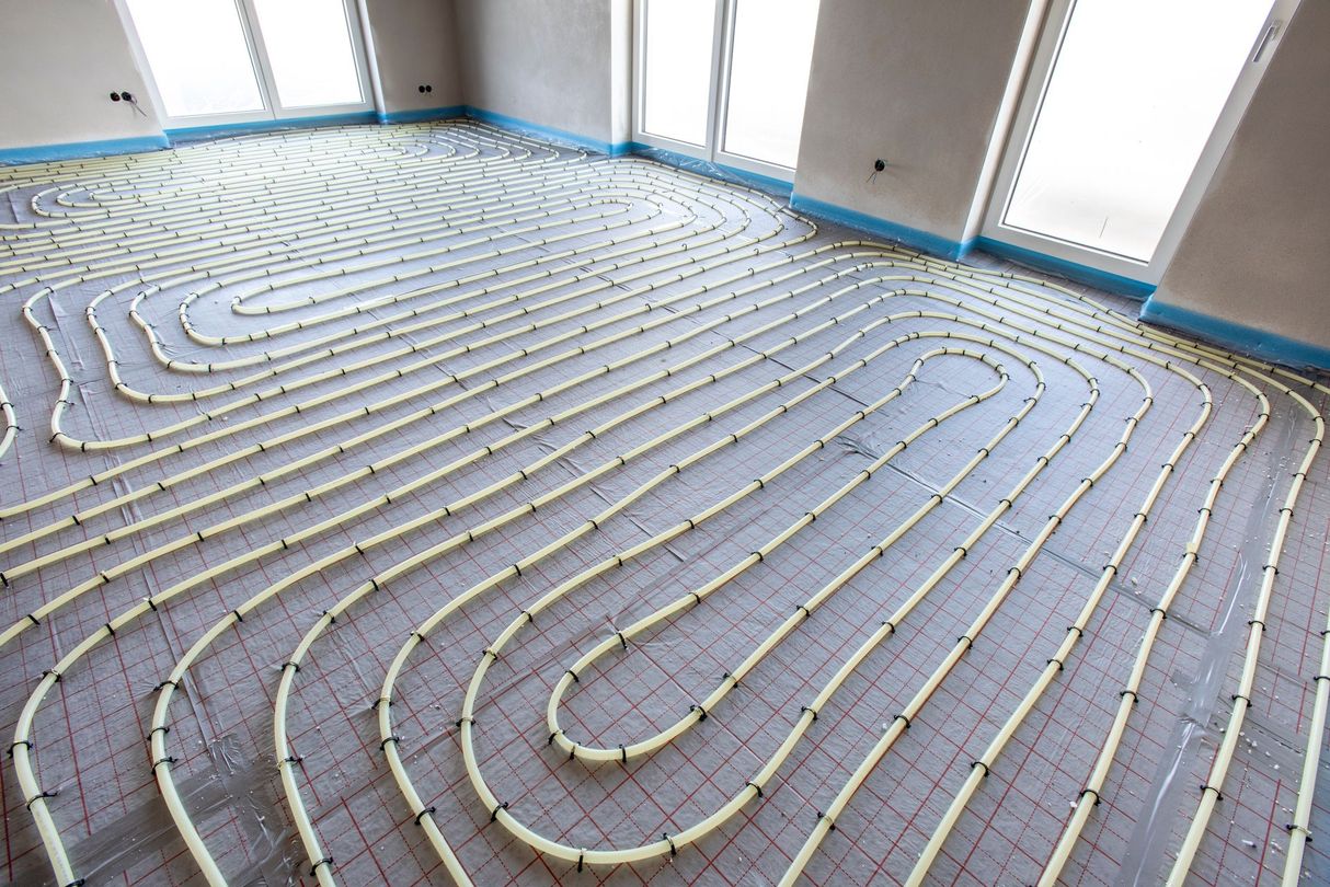 Tuyaux disposés sur un sol en béton, pour l'installation d'un chauffage au sol.