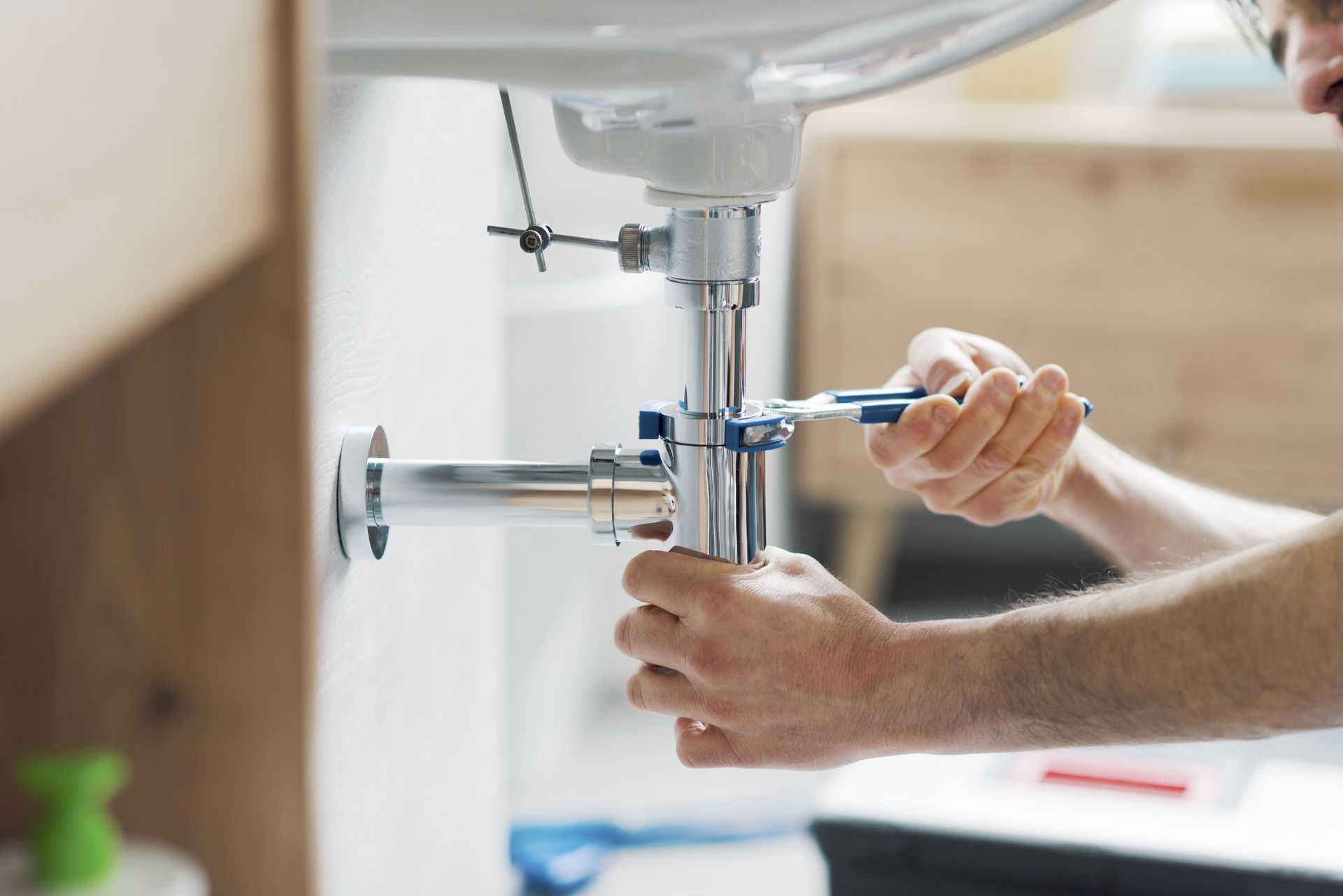 Un plombier utilise une clé pour resserrer un tuyau sous un lavabo blanc.