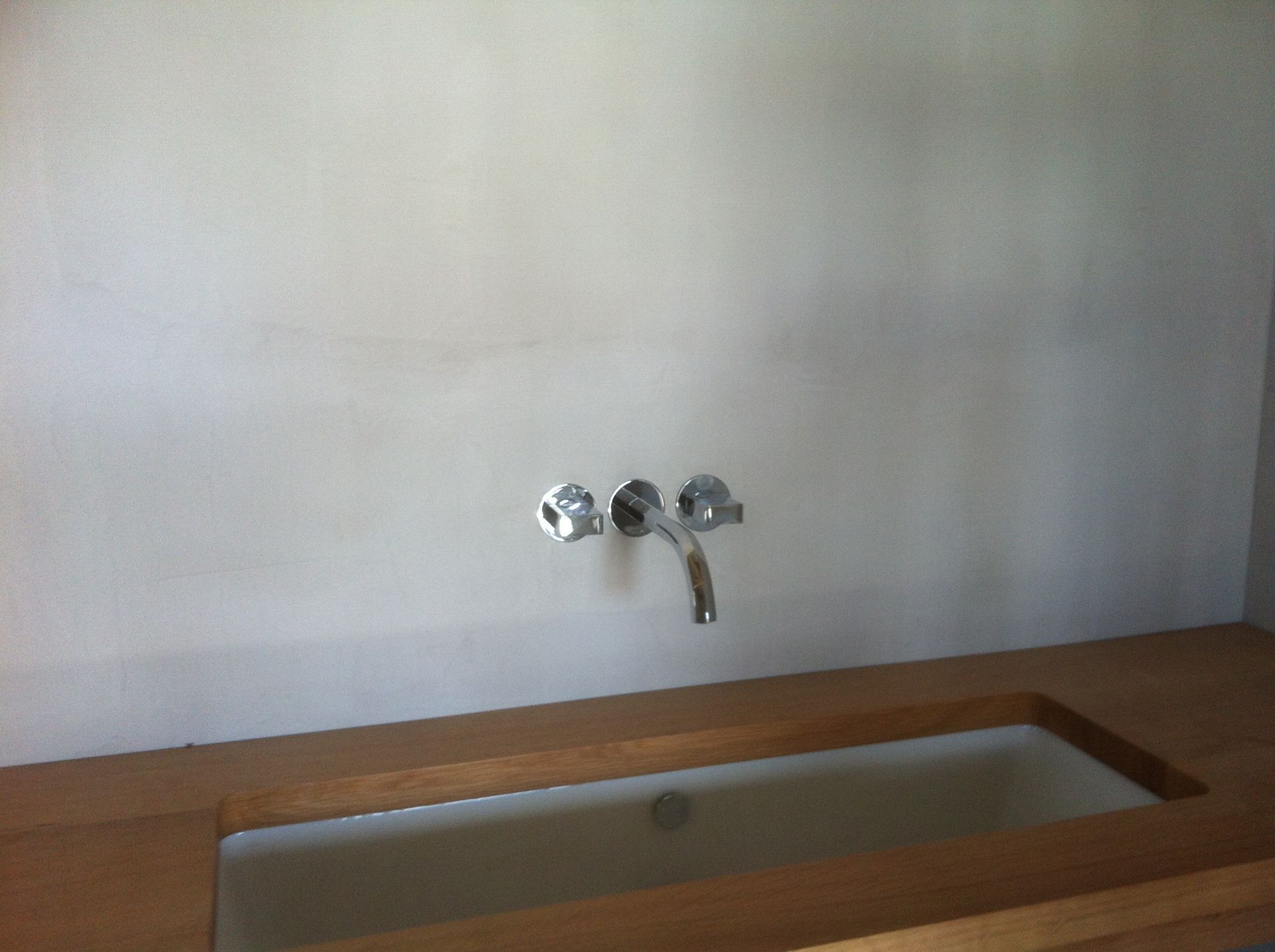 Robinet mural avec lavabo intégré à un plan de travail en bois.