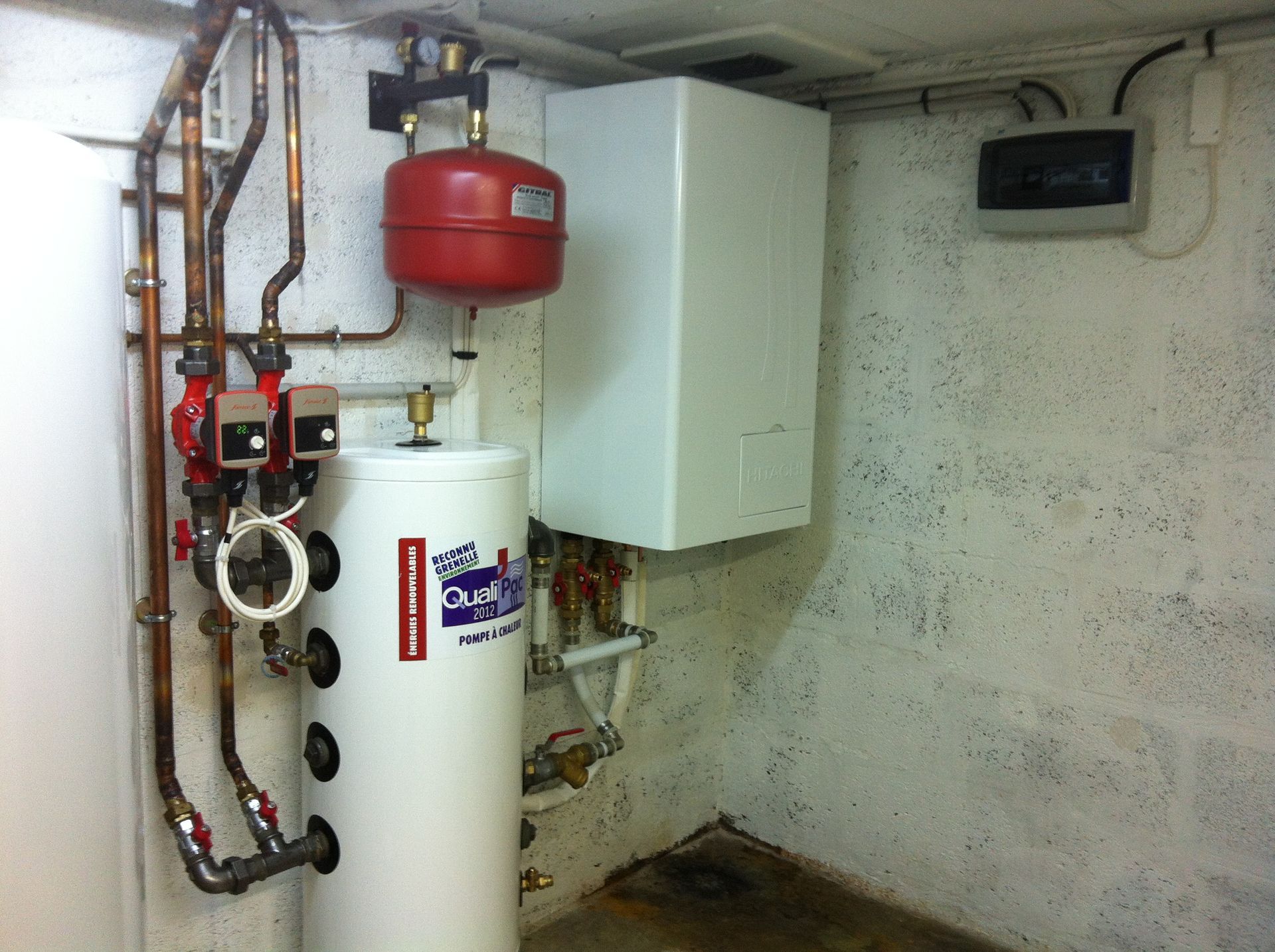 Composants du système de chauffage, notamment chauffe-eau, vase d'expansion rouge et chaudière, situés au sous-sol.