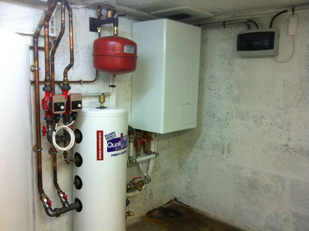 Composants du système de chauffage, notamment chauffe-eau, vase d'expansion rouge et chaudière, situés au sous-sol.