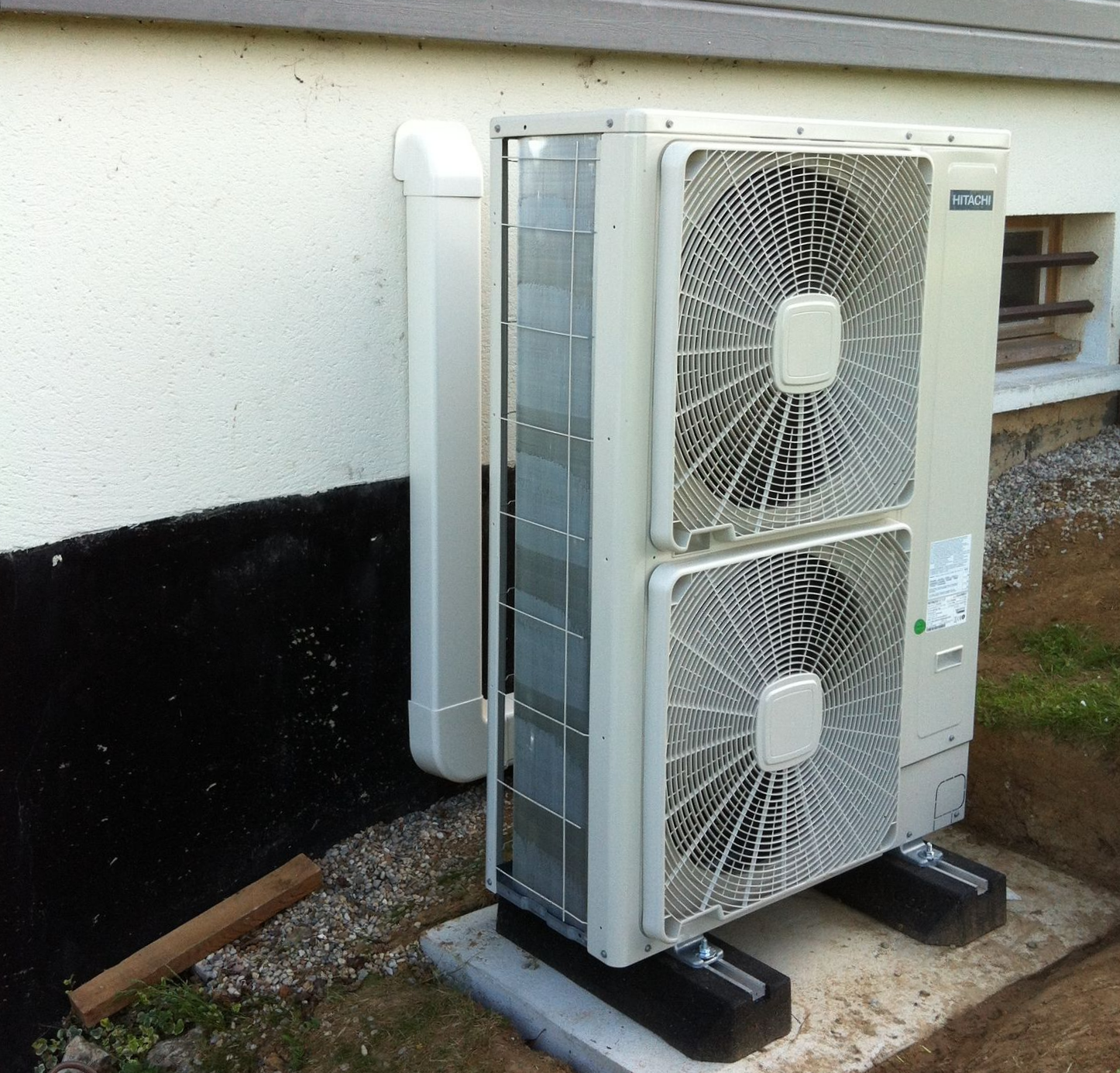 Unité de pompe à chaleur Hitachi, blanche et grise, près d'un bâtiment.
