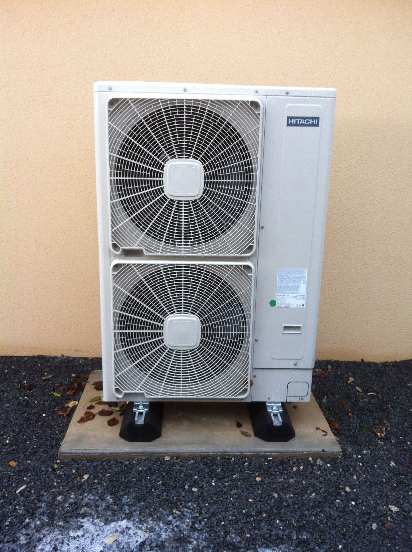 Unité de climatisation sur une dalle de béton, contre un mur beige.