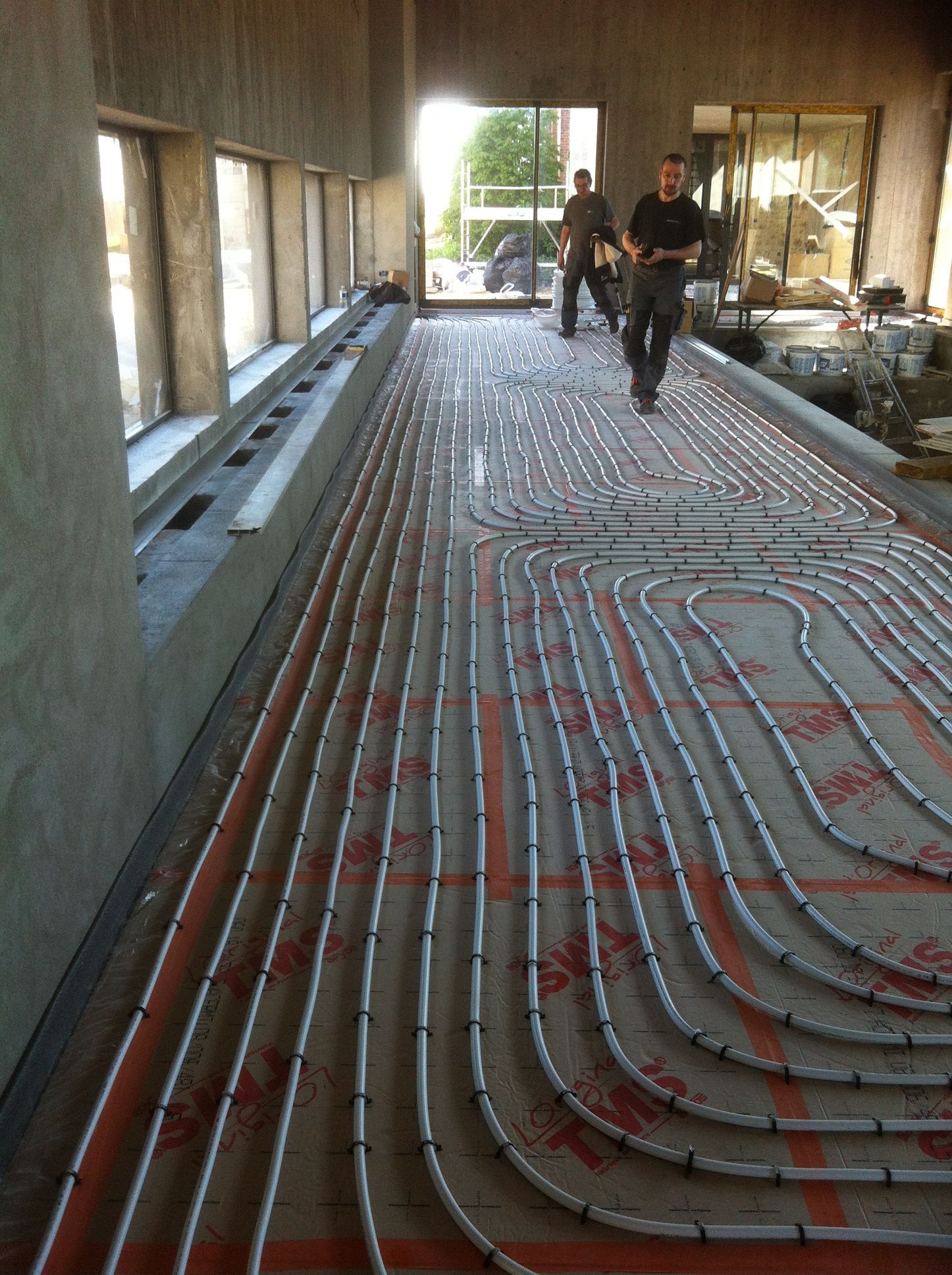 Des tuyaux sont installés au sol, avec deux hommes qui marchent en arrière-plan.