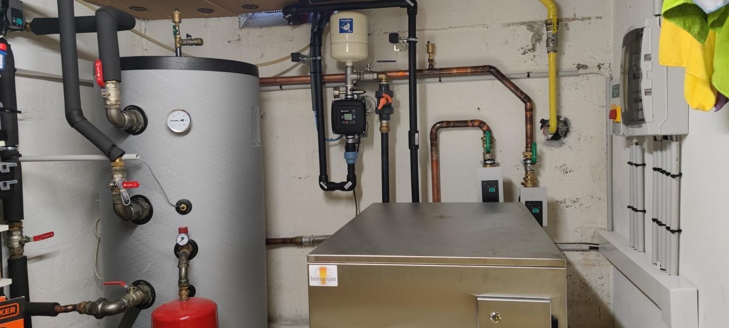 Une buanderie avec un grand chauffe-eau, des tuyaux et un coffre métallique.