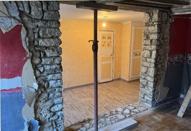 Porte à encadrement de pierre apparente s'ouvrant sur une pièce éclairée avec parquet et portes blanches