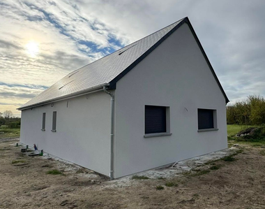 Petite maison blanche au toit de métal gris dans un champ rural sous un ciel nuageux