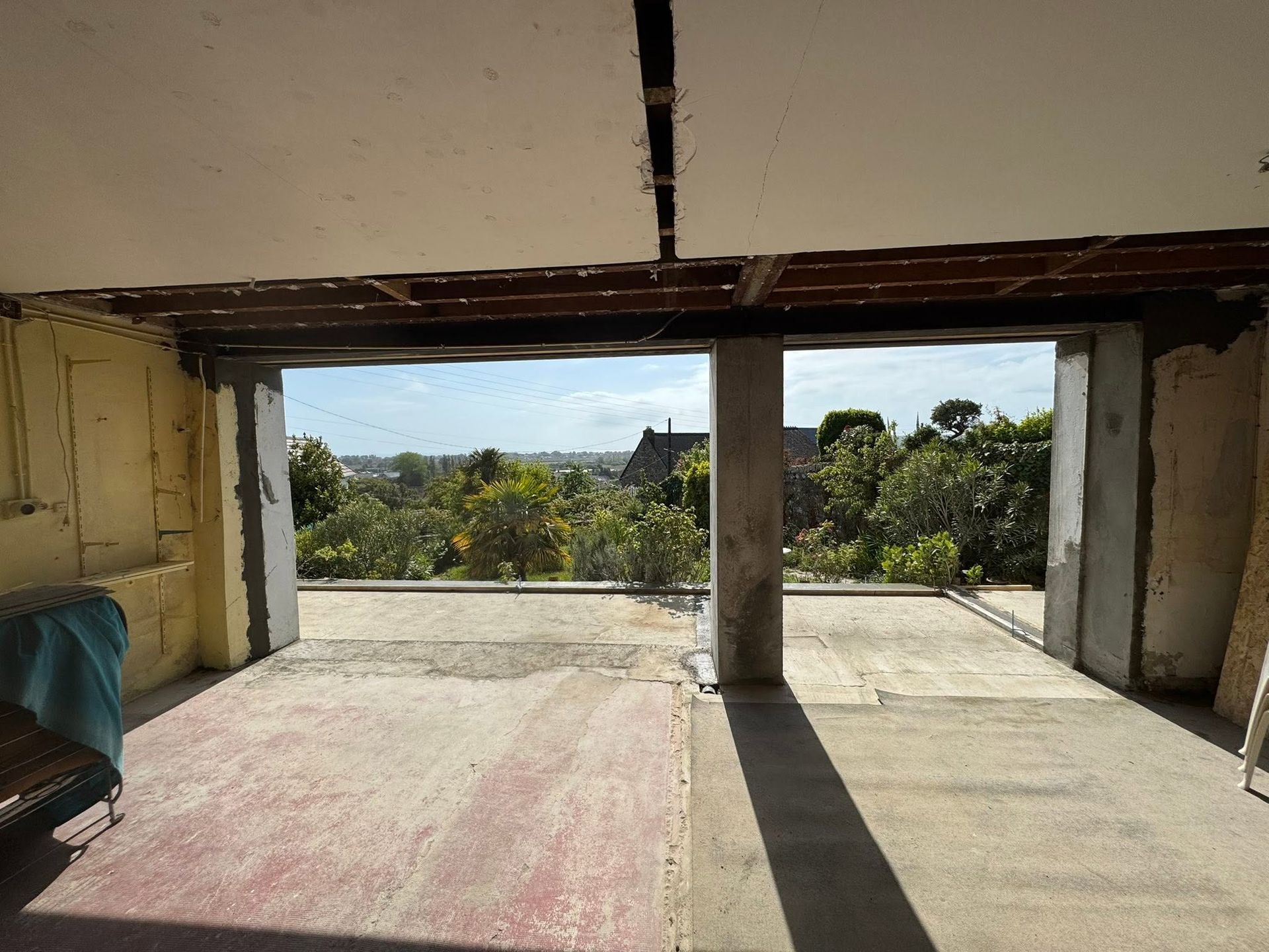 Intérieur de pièce ouverte avec un pilier central, lumière naturelle et vue sur les arbres et les collines à travers le balcon ouvert.