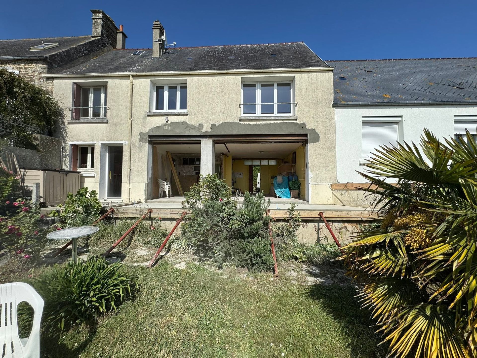 Jardin arrière avec une maison en pierre couleur crème, terrasse, pelouse et plantes en pot ensoleillées