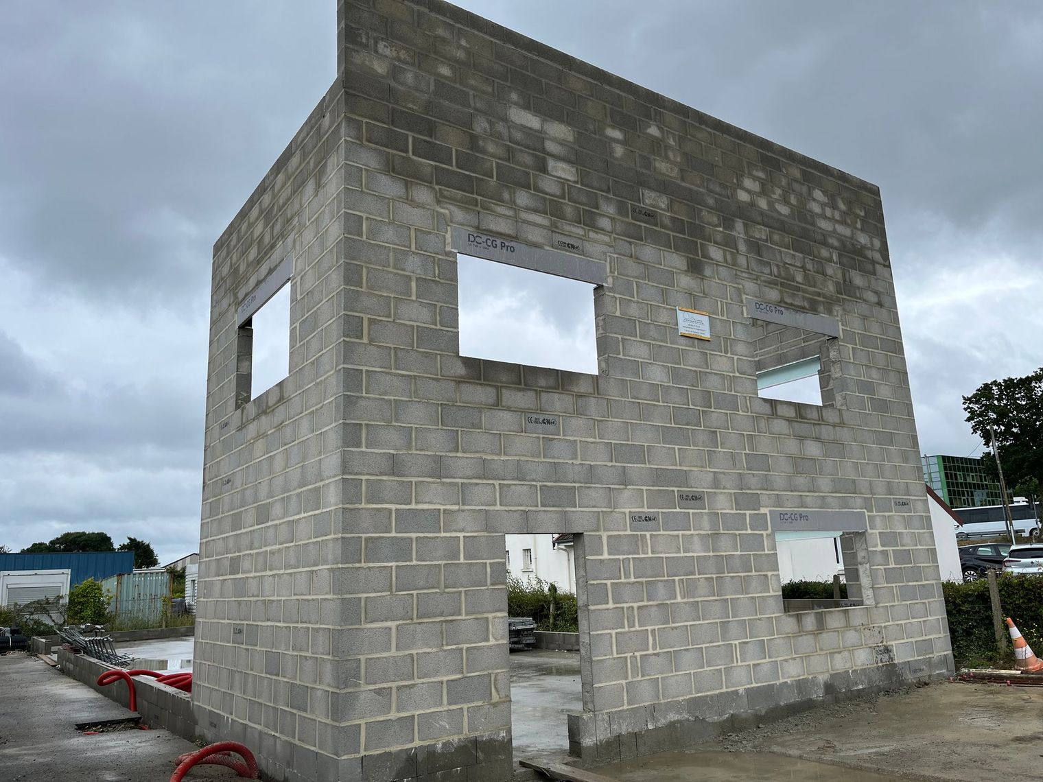 Bâtiment de deux étages en parpaings en construction, avec des ouvertures de fenêtres non finies.