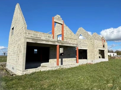 Maison en pierre partiellement construite avec des poutres de soutien orange sous un ciel bleu