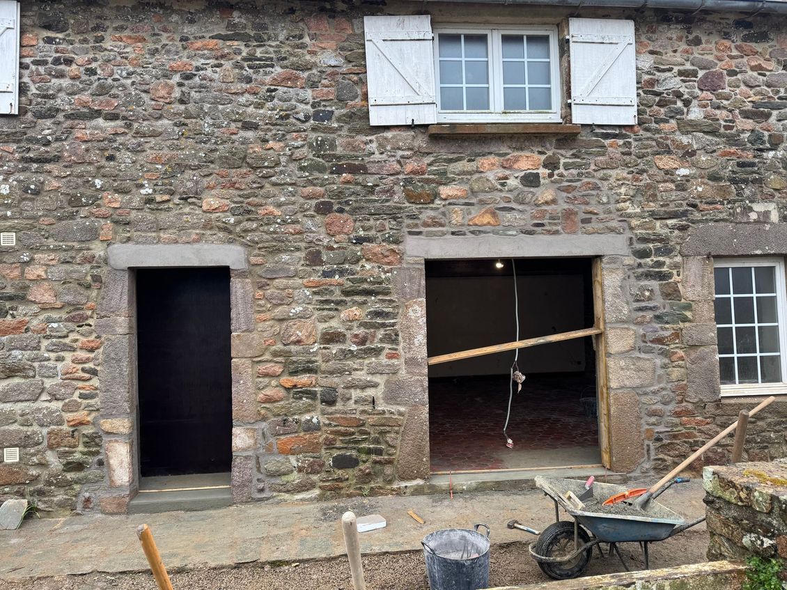 Ancien bâtiment en pierre avec une porte ouverte, une fenêtre brisée et des débris de construction devant.