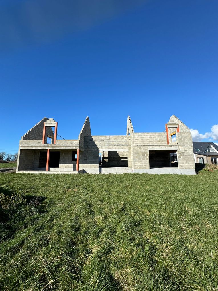 Maison en pierre en construction sur une colline herbeuse sous un ciel bleu clair