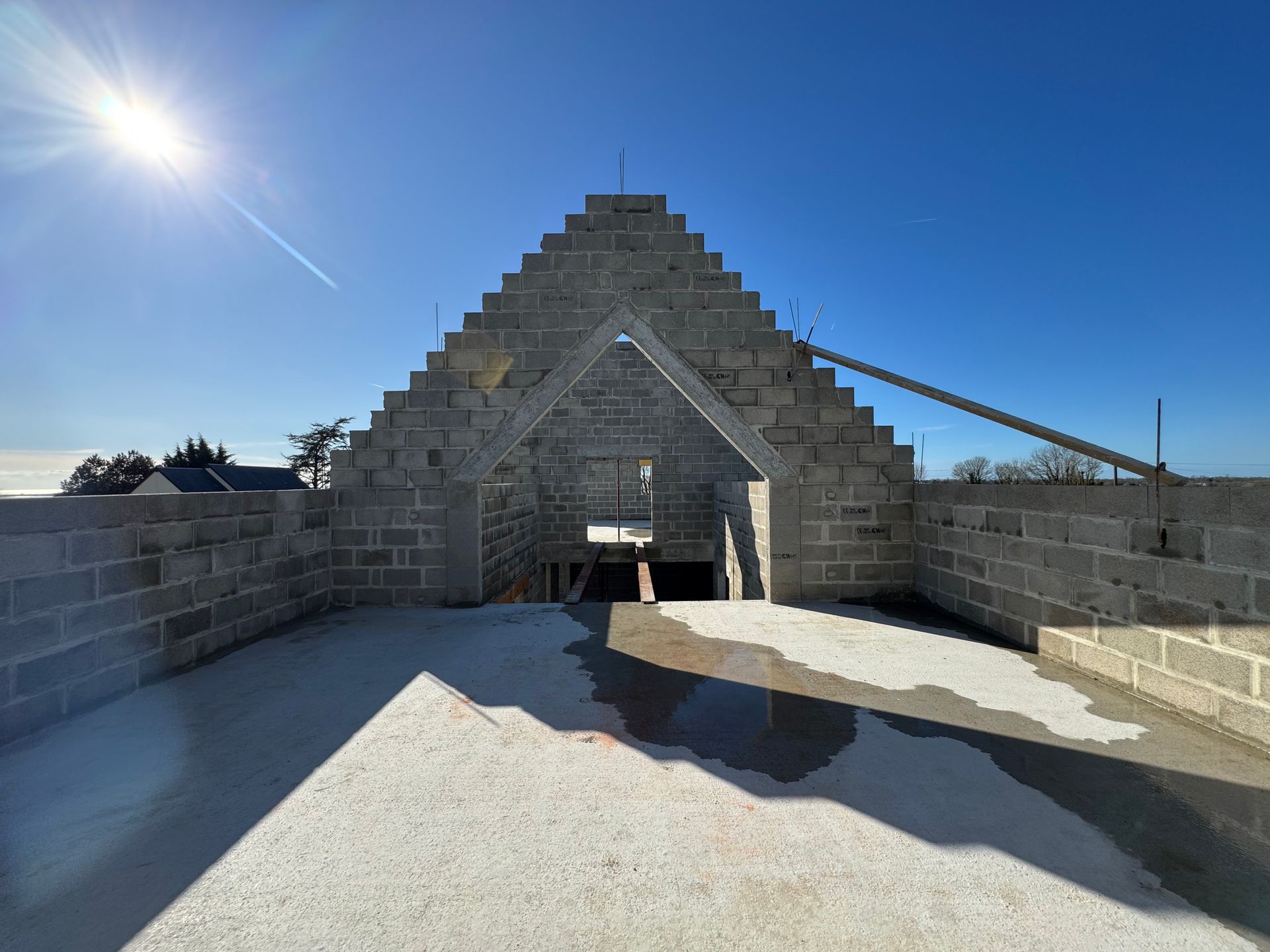 Bâtiment en pierre en construction, avec une ouverture triangulaire sur le toit, soleil éclatant et ciel bleu.