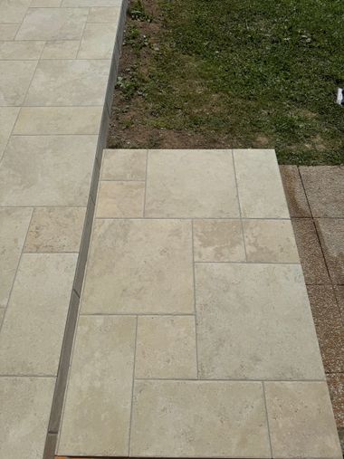 Terrasse en pierre bordant une pelouse, montrant des dalles de pavage beige clair et un bord de trottoir.
