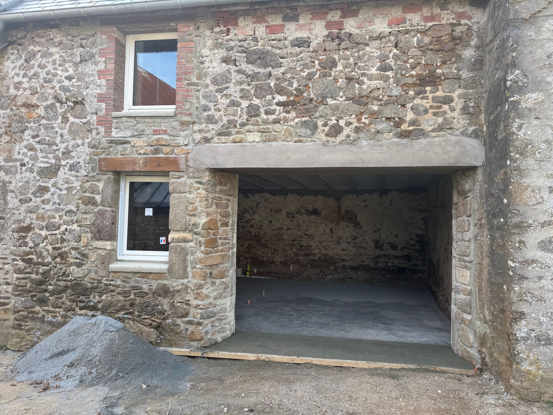 Bâtiment en pierre avec entrée de garage ouverte et petite fenêtre au-dessus.