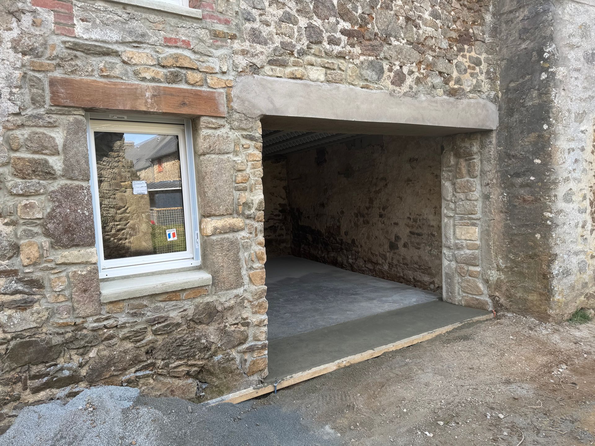 Façade en pierre avec une petite fenêtre et une grande porte ouverte de type garage.