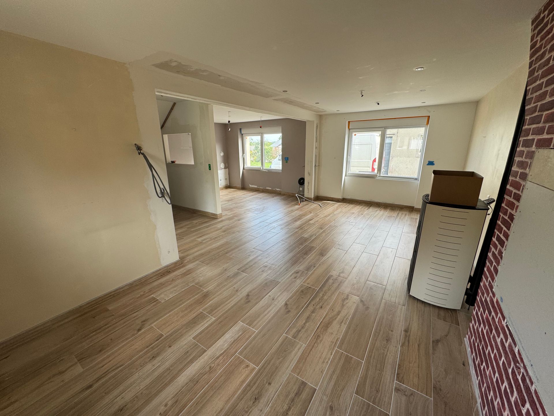 Pièce vide avec parquet, murs beiges et grandes fenêtres dans un intérieur lumineux et inachevé.